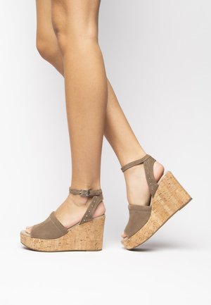 Brown suede wedge sandals with cork platform, open toe design, ankle strap with buckle, and decorative studs along the strap.