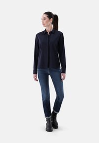 Navy button-up shirt with long sleeves, paired with denim jeans. Black ankle boots with a textured sole complete the look.
