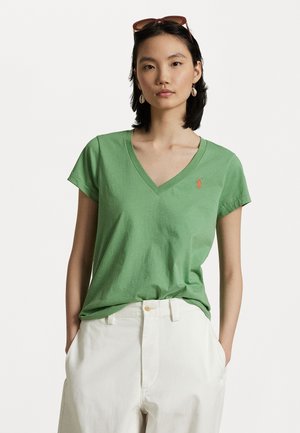 Groen katoenen v-hals t-shirt met korte mouwen, voorzien van een klein oranje logo op de linkerborst. Draagt men met witte, hoog waisted broek.