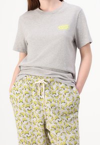 Grå t-shirt med kort ärm och en gul logotyp på bröstet, tillsammans med grå sweatpants med ett bananmönster och dragsko i midjan.