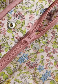 Tissu à motif floral aux couleurs pastel avec des dessins rose, bleu et vert, accompagné d'une fermeture éclair rose et d'un détail de bouton-pression métallique.