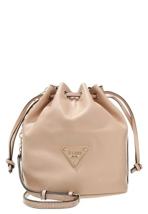 Beige leren boodschappentas met trekkoord, verstelbare riem en driehoekig gouden Guess-logo op de voorkant.