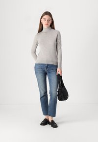 Helehall turtleneck-kampsun, keha lähedane disain, koos keskmise sinise sirge teksapaariga. Must kudumine käekott ja mustad libisemisega kingad.