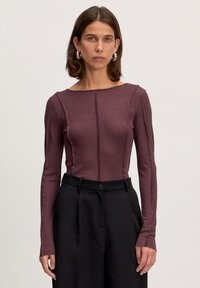 Langsleeve aangesloten top in diep bordeaux ribstof, met een bootnek en verticale naaddetail, gecombineerd met hoge zwarte broeken.
