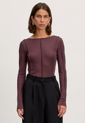 Langsleeve aangesloten top in diep bordeaux ribstof, met een bootnek en verticale naaddetail, gecombineerd met hoge zwarte broeken.