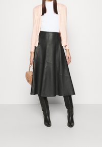 Falda de cuero negra con un diseño acampanado, combinada con una blusa ajustada blanca y un cárdigan rosa claro. Botas negras hasta la rodilla completan el look.