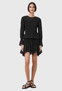 Schwarzes Kleid mit einer gerafften Brustpartie, langen Ärmeln, mehrlagigem Taillenabschluss und einem ausgestellten Rock. Leichter Stoff mit einer strukturierten Oberfläche.