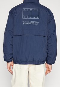 Mörkblå puffjacka med elastisk nederkant, har en logotyptryck på baksidan, tillverkad av lätt material och har en avslappnad passform.