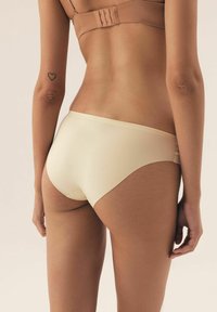 Beżowa, bezszwowa bielizna o niskim stanie, gładkiej fakturze i minimalnym pokryciu, z subtelnymi detalami szycia.