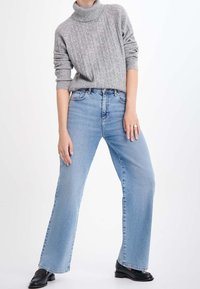 Szary prążkowany sweter z golfem zestawiony z jasnoniebieskimi dżinsami o prostych nogawkach, z wysokim stanem i bez widocznych zdobień. Czarne loafersy.