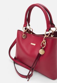 Sac à main en cuir rouge avec poignées doubles, quincaillerie dorée et étiquette amovible. Présente une finition texturée et une forme structurée.
