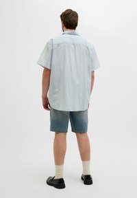 Camisa de botones de manga corta con rayas azul claro sobre un fondo blanco, combinada con pantalones cortos de mezclilla, zapatos negros y calcetines blancos.