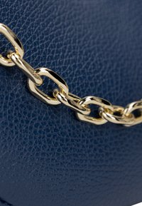 Borsa in pelle color blu navy con una finitura testurizzata e tracolla in catena dorata. I link della catena sono lisci e lucidi, creando un contrasto con la superficie.