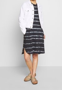 Black tie-dye dress with white stripes, accompanied by a white denim jacket and beige sandals featuring double buckles.