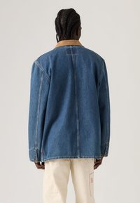 Τζιν μπουφάν σε μπλε με γιακά από καφέ κορντούρο. Διαθέτει άνετη γραμμή και εμφανείς ραφές κατά μήκος των ραφών. Κουμπιά στα μανίκια και στο τελείωμα.