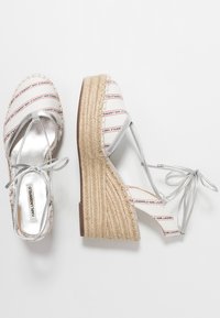 Srebrne sandały na koturnie z espadryli z plecioną platformą z juty, wzorzystymi paskami z tkaniny oraz błyszczącym metalicznym wykończeniem na wkładce.