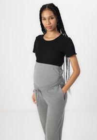 Melna ribota kr短ām piedurknēm tops, savienots ar pelēkiem augsto jostasvietu joggeriem, kas aprīkoti ar piespraustu jostas mietu un sānu kabatām, kas paredzēti komfortam.