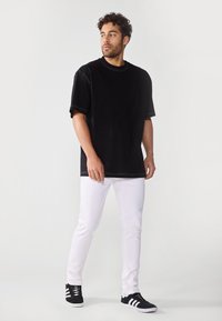 Sort oversized t-shirt i blødt stof med korte ærmer, som er sat sammen med tætsiddende hvide jeans og sorte sneakers med hvide detaljer.