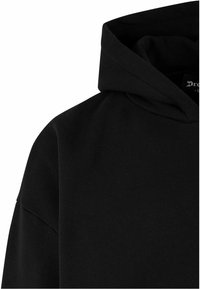 Schwarzer Hoodie aus Baumwolle, mit einer großen Kapuze, weichem Griff und minimalistischem Design, ohne sichtbare Muster oder Metallteile.