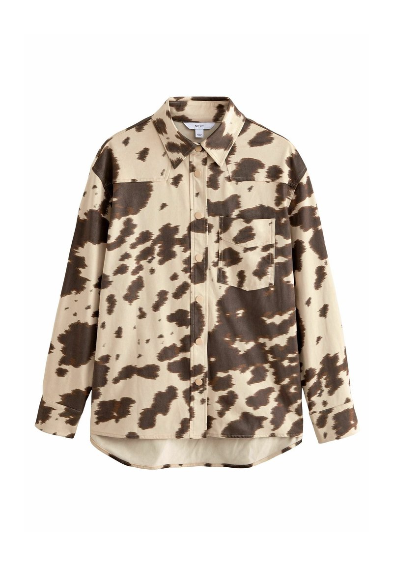 Chemise beige à boutons avec motif irrégulier en peau de vache brun foncé, manches longues, col pointu et poche poitrine sur fond blanc.