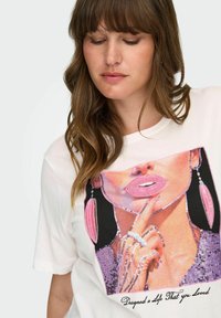 Valkoinen graafinen t-paita, jossa on värikäs suu- ja käsi-kuviointi, tavara-flitterit, mustat aksentit ja teksti "Suunnittelin elämän, jonka rakastit."