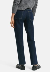 Mörkblå jeans i denim med rak benprofil, med bakfickor och kontrasterande gul sömnad. Kombinerat med svarta skor.