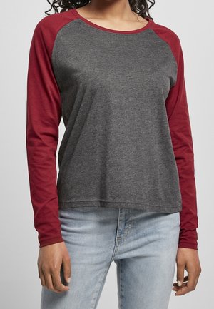 Persoon draagt een longsleeve raglanshirt met een donkergrijze romp en wijnrode mouwen, gecombineerd met lichtblauwe spijkerbroek.