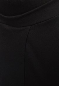 Calças de tecido elástico pretas com uma cintura lisa e superfície texturizada, apresentando um detalhe de costura na lateral para um design adicional.
