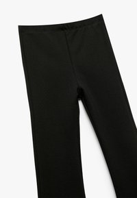 Zwarte leggings van glad, rekbaar materiaal. Kenmerken zijn een hoge taille en een aansluitend ontwerp, met verticale naden voor definitie.