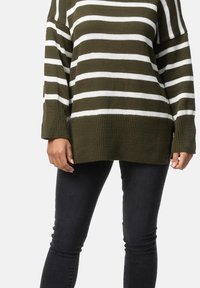 Maglione a righe caratterizzato da colori verde oliva e bianco, tessuto lavorato a maglia, maniche larghe e vestibilità rilassata, abbinato a jeans aderenti neri.