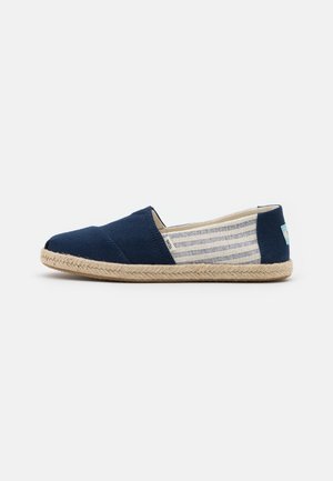 Chaussure slip-on bleu marine avec tissu rayé sur les côtés et semelle en corde beige, vue de profil sur fond blanc.