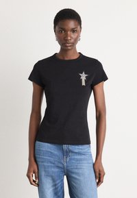 Black short-sleeve t-shirt with a round neck, featuring silver star embroidery on the left chest and a fitted silhouette. Blue jeans worn.