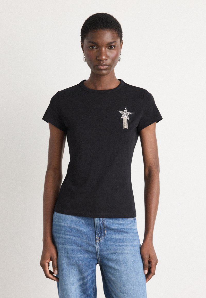 Black short-sleeve t-shirt with a round neck, featuring silver star embroidery on the left chest and a fitted silhouette. Blue jeans worn.