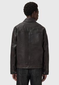 Veste en cuir marron avec une texture lisse, fermetures à bouton et col classique. Présente une coupe ajustée et des coutures piquées.