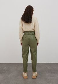 Groene faux leren hoge taille broek met een riemontwerp, gedragen bij een beige geweven trui en crèmekleurige sneakers.