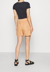 Shorts à motifs pêches avec une finition texturée et une taille élastique, associés à un t-shirt noir ajusté et des sandales noires à lanières.