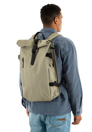 Sac à dos à roulettes en matériau imperméable beige, avec des sangles ajustables, un design à rabat roulé et une poche zippée à l'avant.