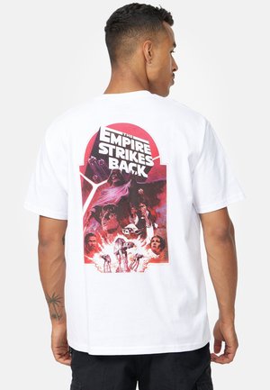 T-shirt bianco in cotone con una stampa grafica colorata sul retro, che mostra personaggi e scene da "L'Impero colpisce ancora."