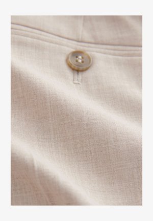 Svetlo bež tkanina z rahlo teksturo, z rjavim gumbom pritrjenim na sredini. Približna slika mehkih, gladkih materialov.