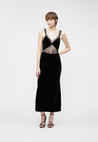 Μαύρο βελούδινο βραδινό φόρεμα με δαντελένιες λεπτομέρειες στο μπούστο, με λεπτές τιράντες και στενή γραμμή που φτάνει μέχρι το πάτωμα.