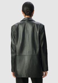 Blazer in pelle nera con una texture liscia, un'unica apertura sul retro e spalle definite; progettato con maniche lunghe e colletto classico.