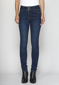 Jeans skinny de color azul oscuro, hechos de mezclilla, con una cintura alta, bolsillos frontales con herrajes dorados y un detalle de costura mínima.