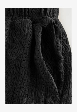 Mustreeritud musta kangast, millel on teemantmuster koos reljeefsete detailidega ja avatud õmblustega. Pehme, elastse vöökohtaga, mis tagab paindlikkuse.