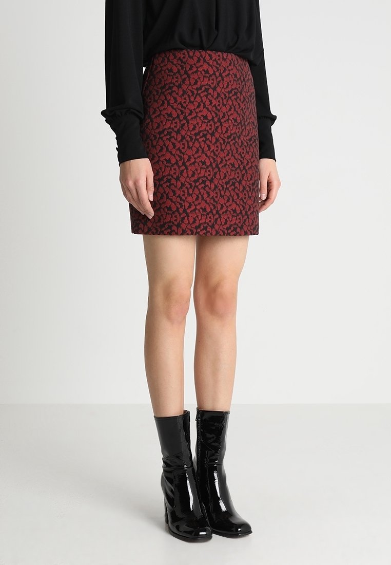Roter und schwarzer gemusterter Rock mit schmalem Schnitt. Getragen mit einem schwarzen Oberteil mit langen Ärmeln und glänzenden schwarzen Stiefeletten. Glatte Textur.