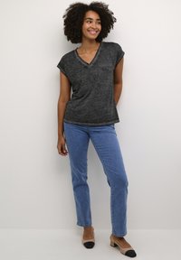 T-shirt noir à col en V avec des manches courtes retroussées, doté d'une poche poitrine. Associé à un jean droit bleu clair et des ballerines bicolores.