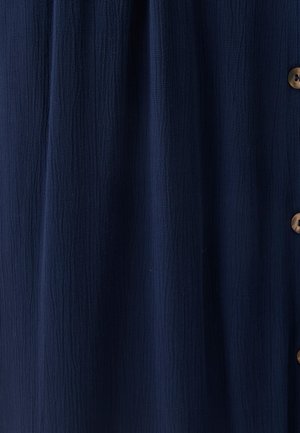 Tessuto blu navy strutturato con pieghe verticali e vista parziale di quattro bottoni marroni sul lato destro.