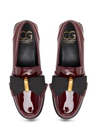Mocassini in pelle patinata bordeaux con un fiocco in tessuto nero e dettagli in oro. Punta arrotondata e superficie liscia con una leggera lucentezza.