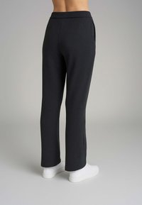 Pantaloni della tuta neri a sigaretta con una texture liscia, dotati di vita alta e tasche laterali, abbinati a sneakers bianche.