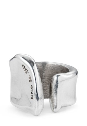 Anillo de metal plateado con una forma orgánica y escultórica. Presenta un interior texturizado y un exterior liso y pulido. Grabado con "UNO de 50".