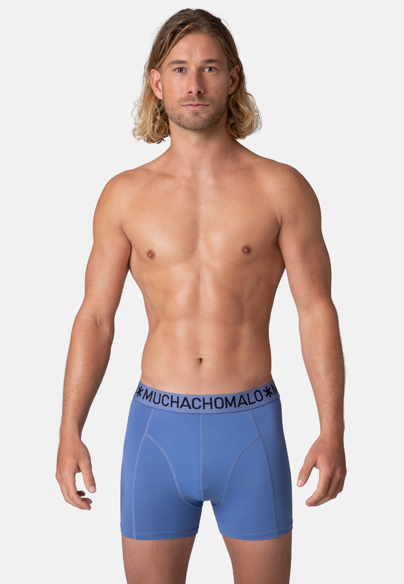Modré boxerky vyrobené z hladkej látky s čiernym elastickým pásom, na ktorom je výrazne napísané meno značky "MUCHACHOMALO".